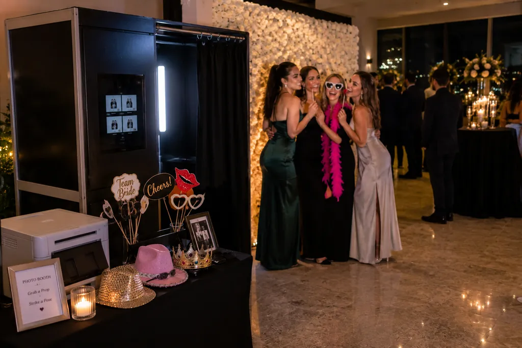 Guests in gowns at the open-air photo booth with a flower wall, props and a print station