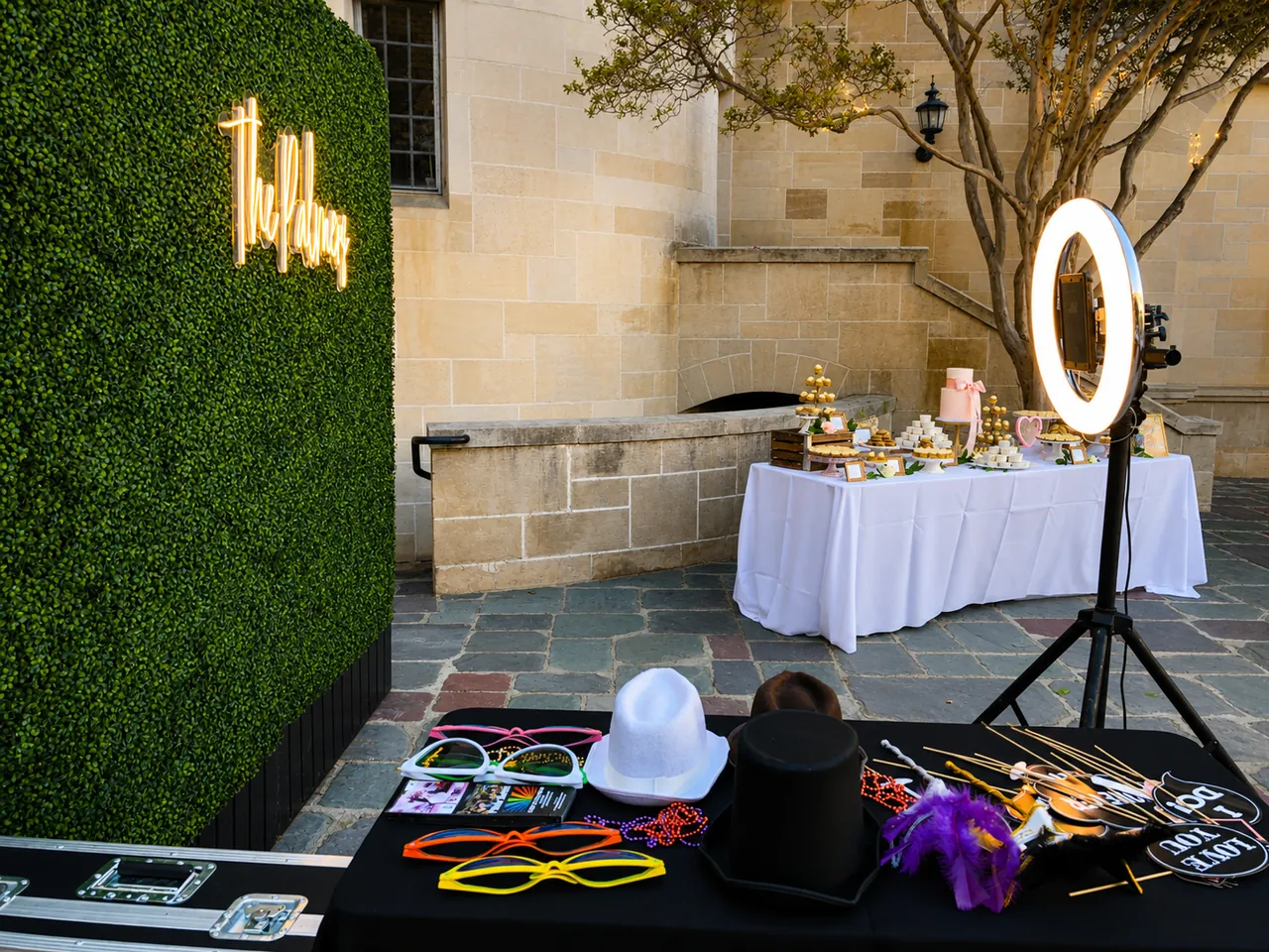 A green hedge backdrop with a neon sign, a ring-light booth and a props table