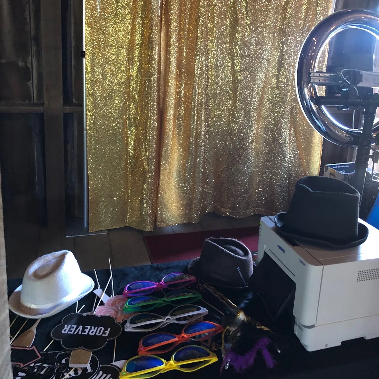 A gold sequin backdrop with a props table, hats and a photo printer